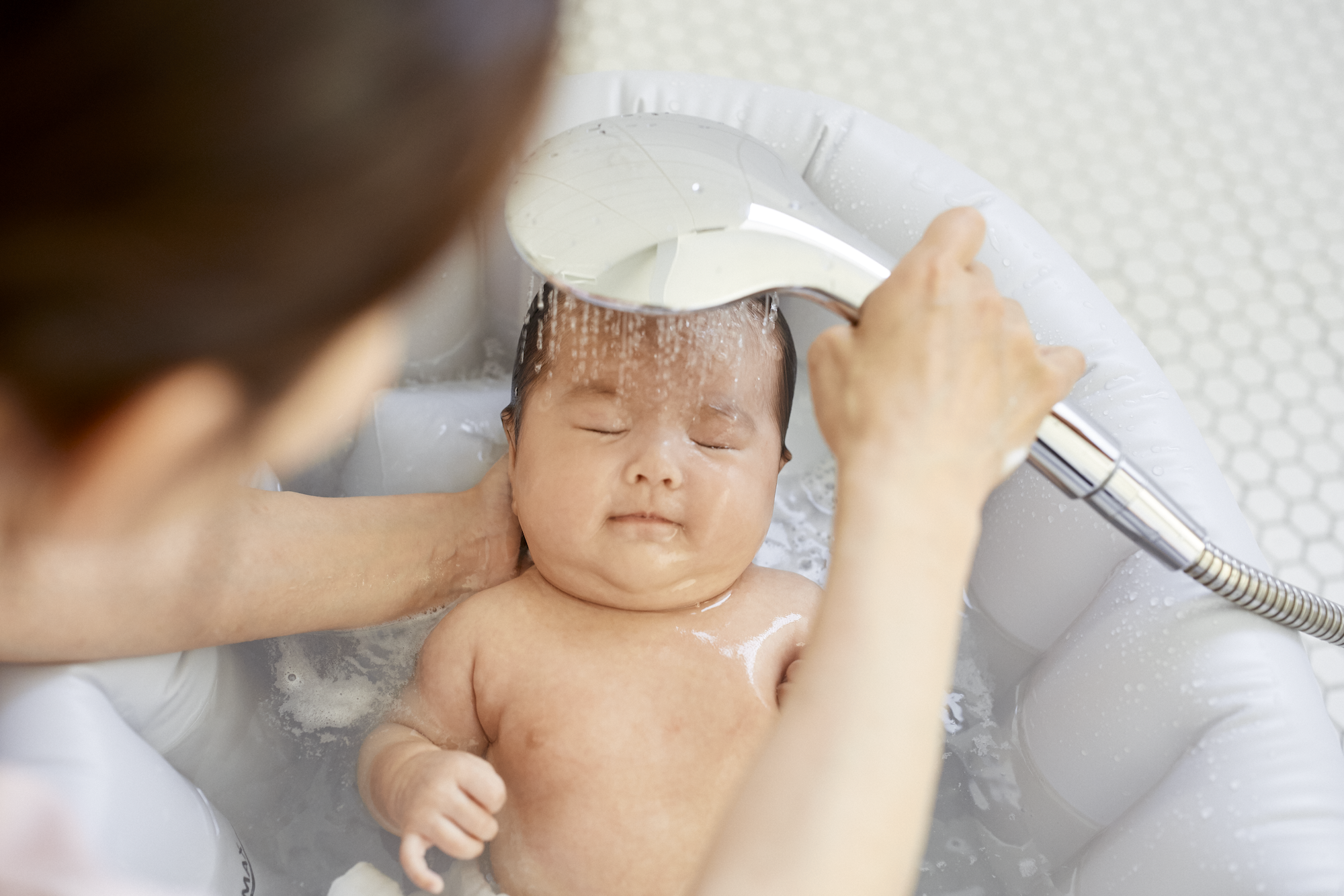 シャワーで泡を流してもらっている赤ちゃん